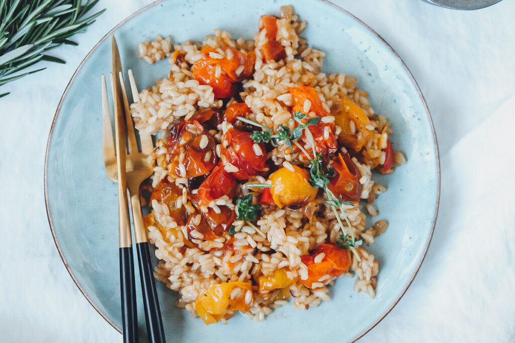 Risotto mit Tomaten auf blauem Teller mit Besteck links