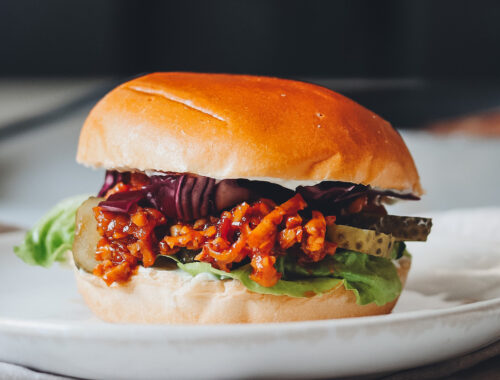 veganer Burger auf hellem Teller vor dunklem Hintergrund
